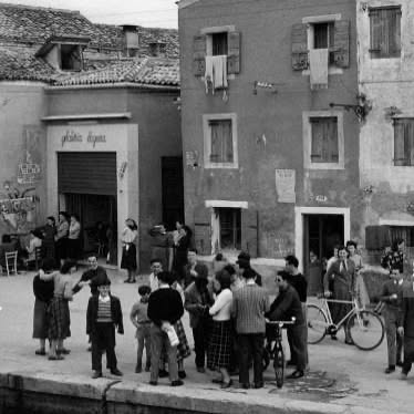 Fotografia d'epoca in bianco e nero: una fondamenta veneziana con una bottega e le persone radunate davanti